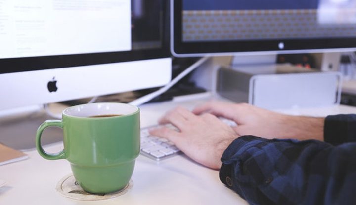 Person typing on computer with a coffee cup on the table
